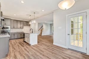 Modern kitchen with gray cabinets, granite countertops, and wood flooring, viewed from adjacent dining area.