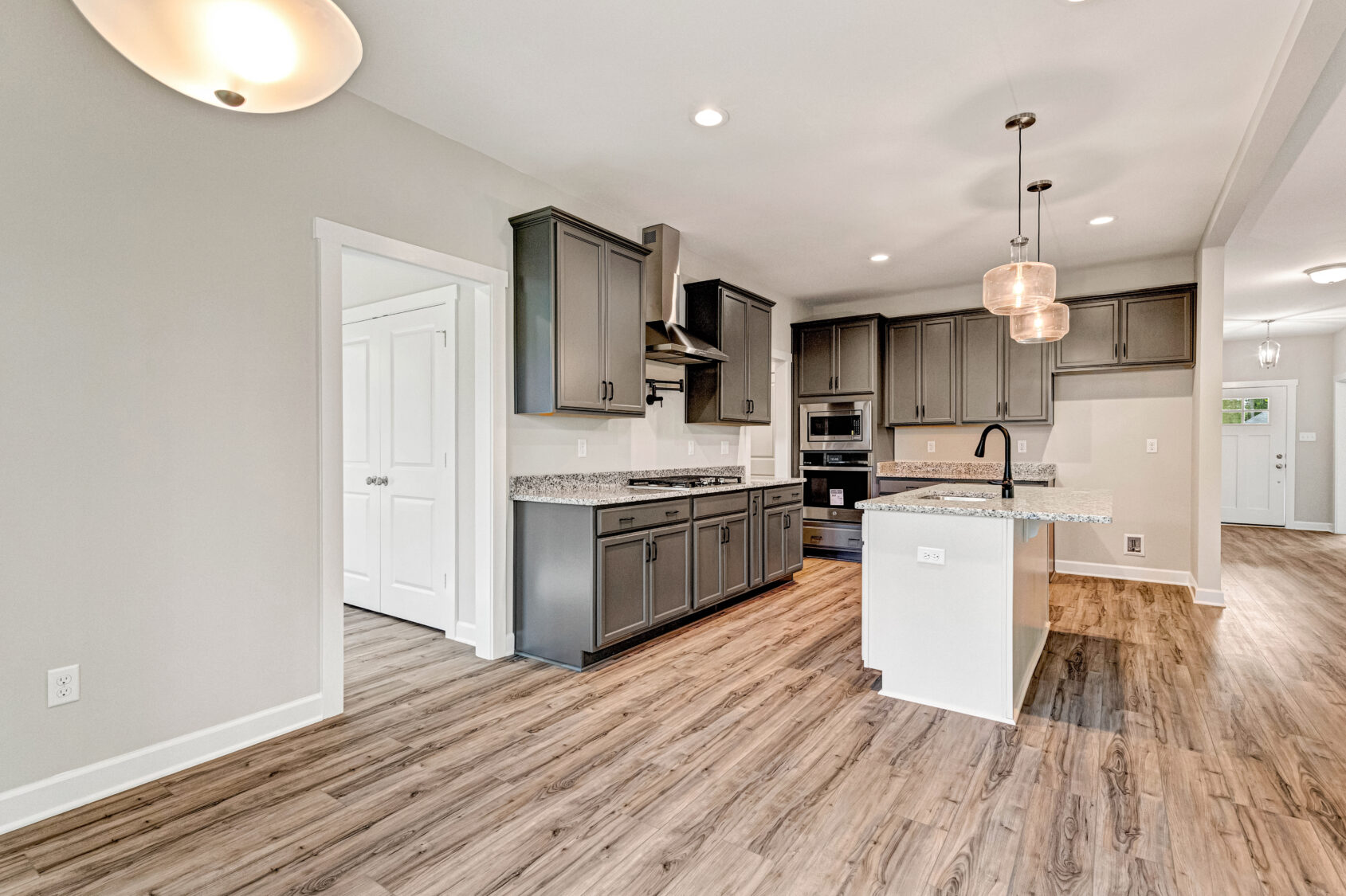 Modern kitchen with gray cabinets, granite countertops, island, pendant lighting, and wood-style flooring.