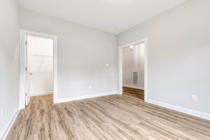 Empty room with light gray walls, wood flooring, and open doorways to a closet and hallway.