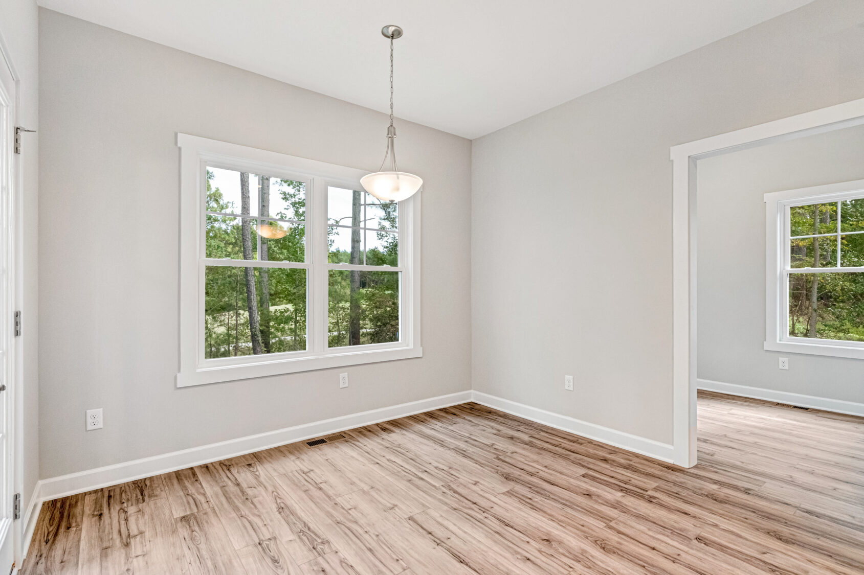 Bright empty room with wood floors, large windows, gray walls, and a ceiling light fixture.
