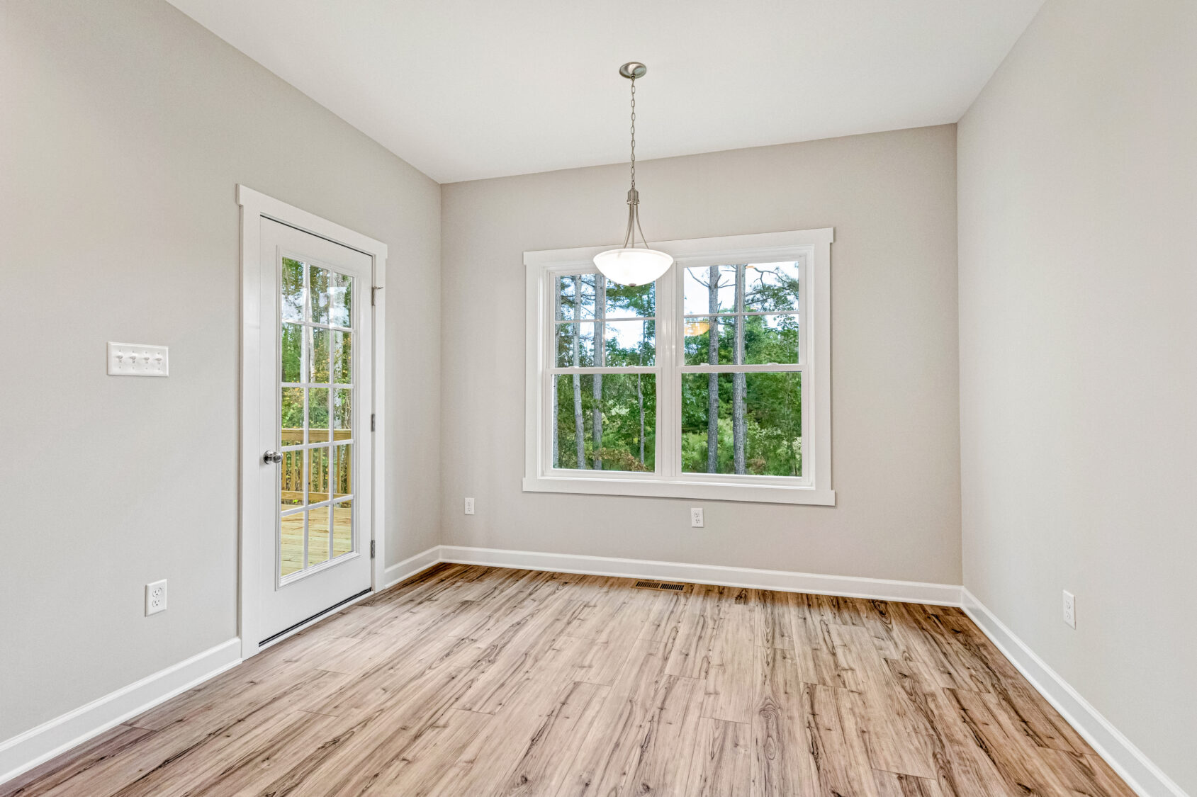 Bright, empty room with wood flooring, large window, glass door, and a hanging light fixture.