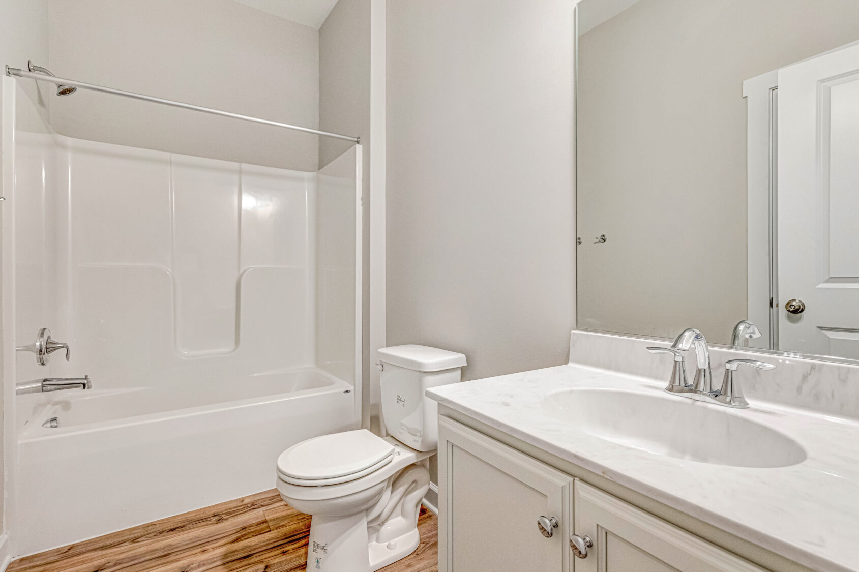 Modern bathroom with a white bathtub, toilet, and sink vanity with a marble countertop and wood-look flooring.