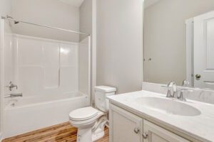 Modern bathroom with a white bathtub, toilet, and sink vanity with a marble countertop and wood-look flooring.