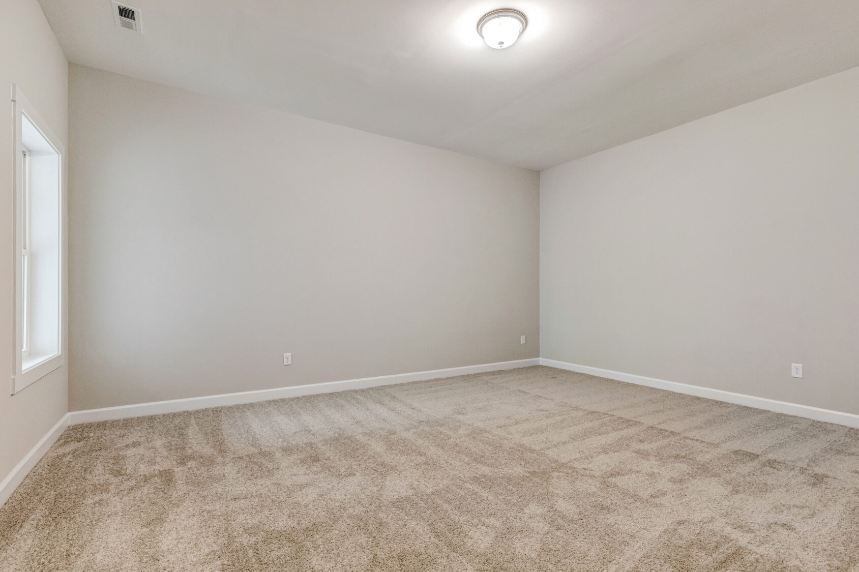 Empty carpeted room with beige walls, white trim, a ceiling light, and a window on the left wall.