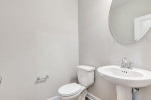 White toilet and pedestal sink in a small bathroom with light gray walls and a round mirror above the sink.
