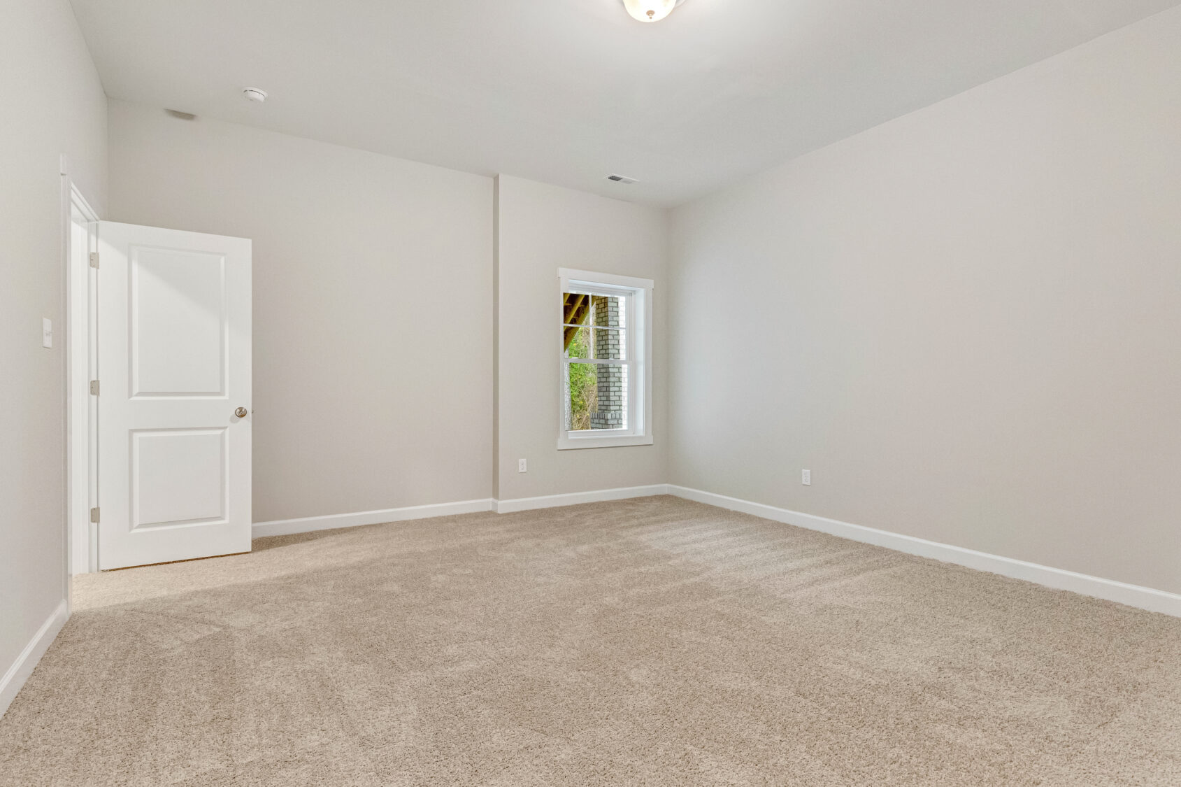 Empty room with beige carpet, light gray walls, a white door, and a window with white blinds.