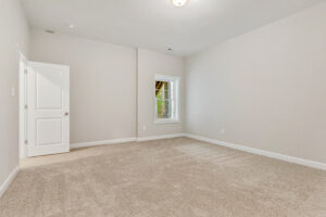 Empty room with beige carpet, light gray walls, a white door, and a window with white blinds.
