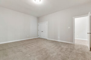 Empty room with beige carpet, light gray walls, a closet with double doors, and an open door to a hallway.