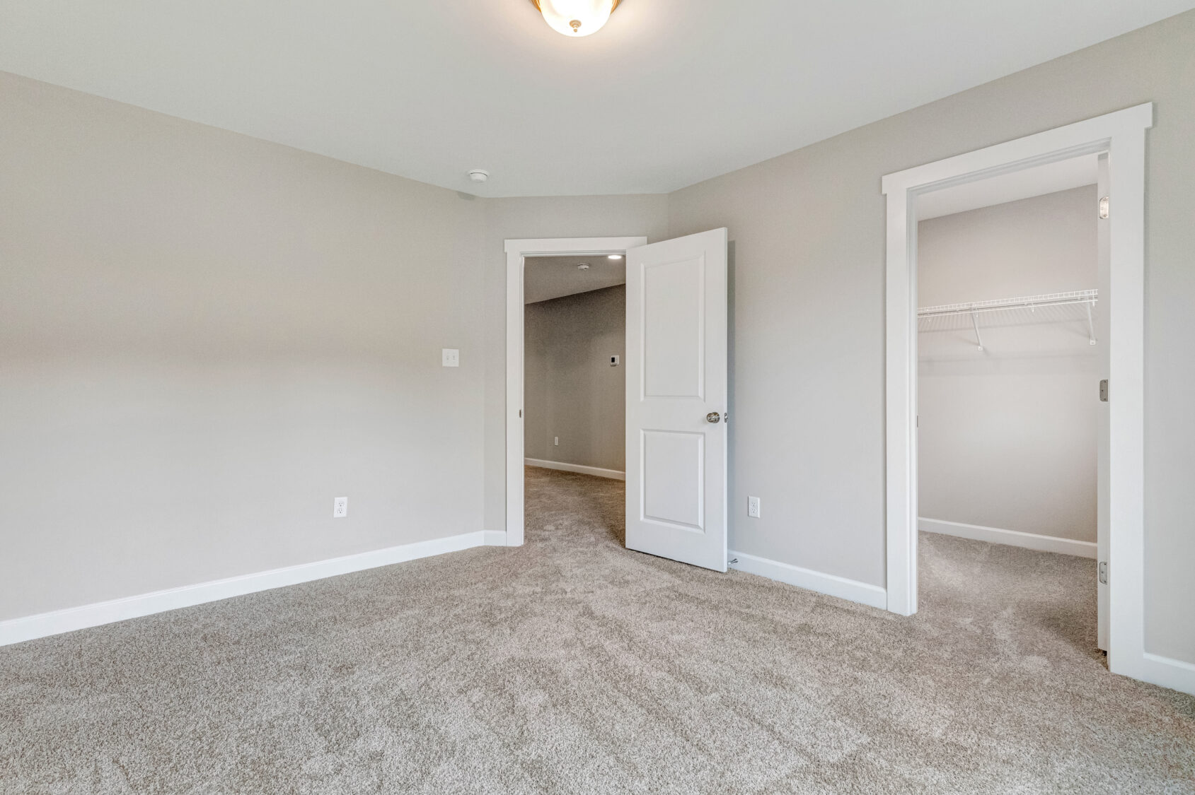 Empty, carpeted bedroom with beige walls, open door, and walk-in closet with wire shelving.