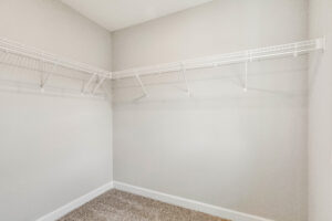 Empty walk-in closet with beige walls, carpet flooring, and white wire shelving on two walls.