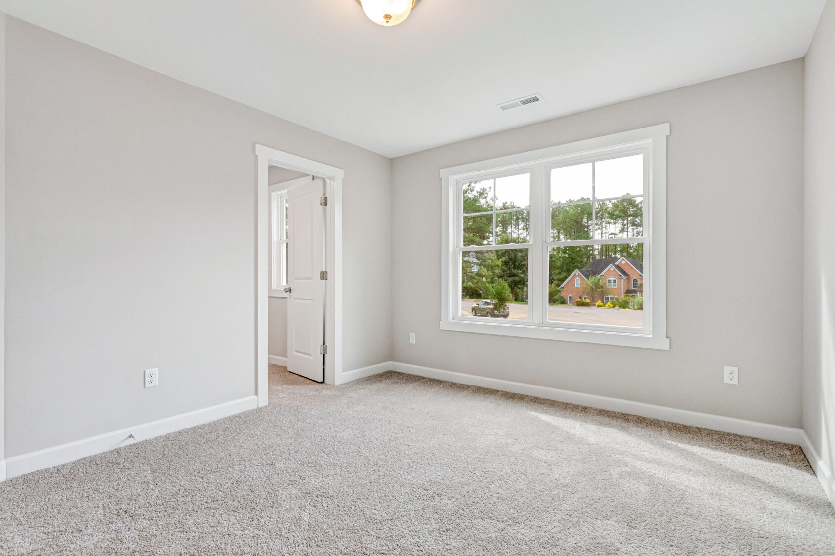 Bright, empty carpeted room with a large window and an open door to an adjacent space.