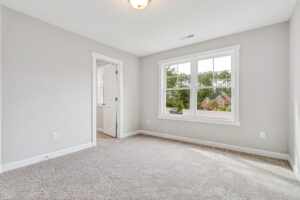 Bright, empty carpeted room with a large window and an open door to an adjacent space.