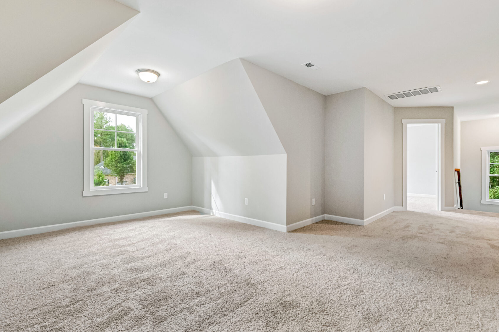 Spacious, carpeted empty room with slanted ceilings, a window, and neutral-colored walls.