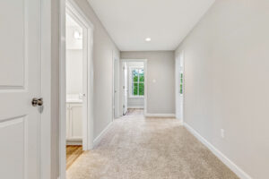 Bright hallway with beige carpet, white walls, open doorways, and a window at the end letting in natural light.