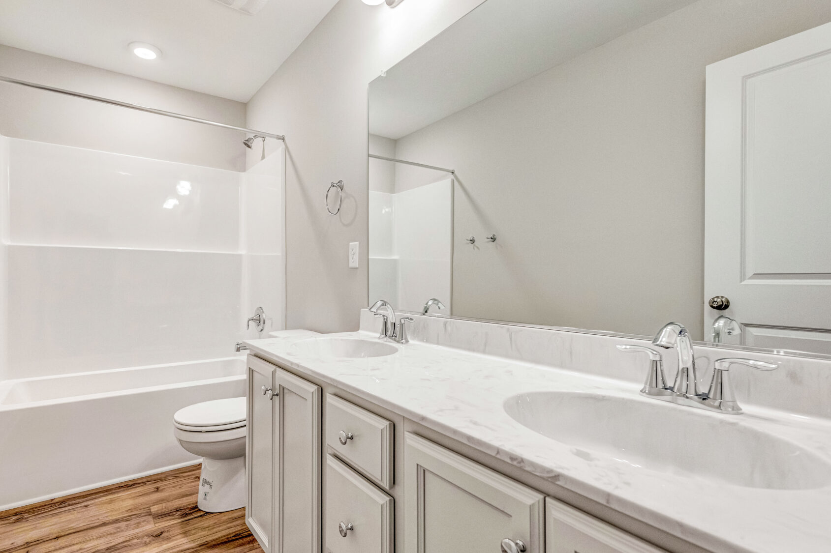 Bright bathroom with double sinks, white cabinets, a bathtub, and wood-look flooring.