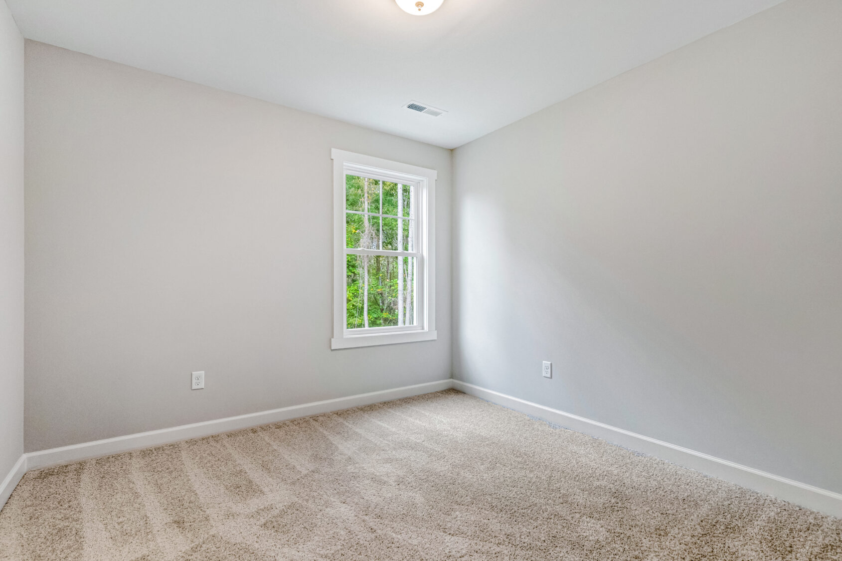 Empty, carpeted room with light gray walls and a single window letting in natural light.