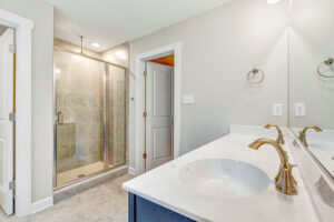 Modern bathroom with double sink vanity, gold faucets, and a glass-enclosed shower.