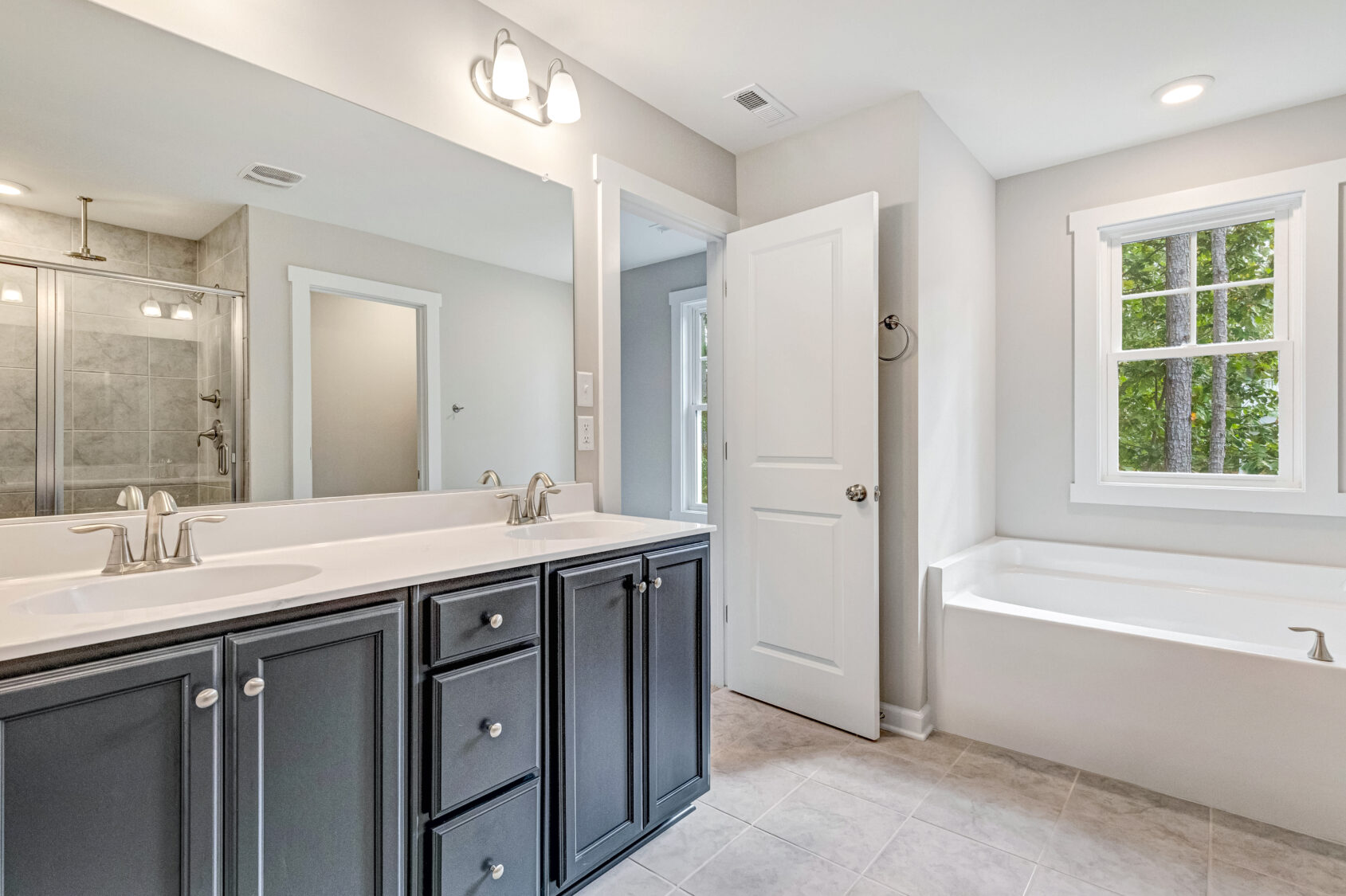 Modern bathroom with double sinks, large mirror, bathtub, window, and glass shower enclosure.