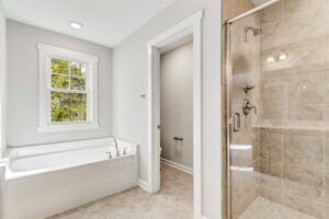 Bright bathroom with a bathtub, separate shower, toilet room, and window with outside view.