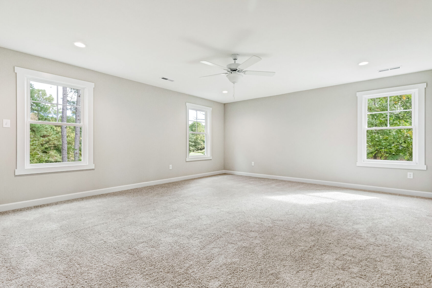 Spacious empty room with beige carpet, white walls, large windows, and a ceiling fan.
