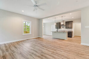 Open living area with wood floors, ceiling fan, and view of a modern kitchen with island and pendant lights.