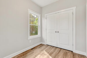 Empty room with light gray walls, wood floor, a window, and double white closet doors.