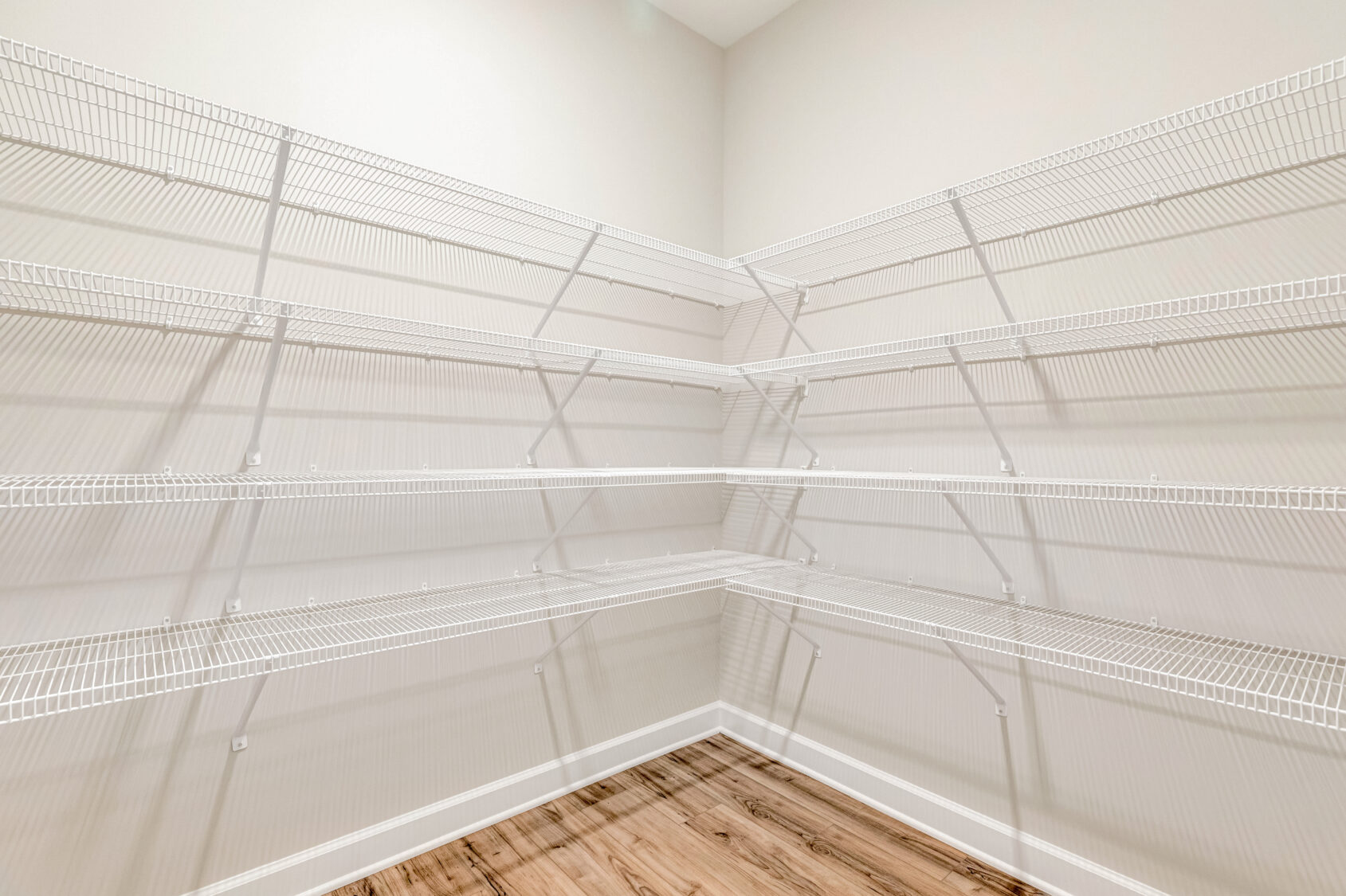 Empty walk-in pantry with white wire shelving and light wood flooring against cream-colored walls.