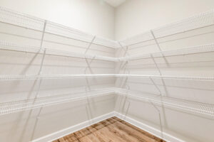 Empty walk-in pantry with white wire shelving and light wood flooring against cream-colored walls.