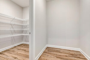 Empty walk-in pantry with white wire shelves on the left and wood flooring throughout the space.