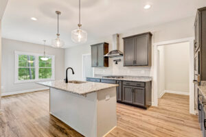 Modern kitchen with gray cabinets, granite countertops, island, pendant lights, and wood flooring.