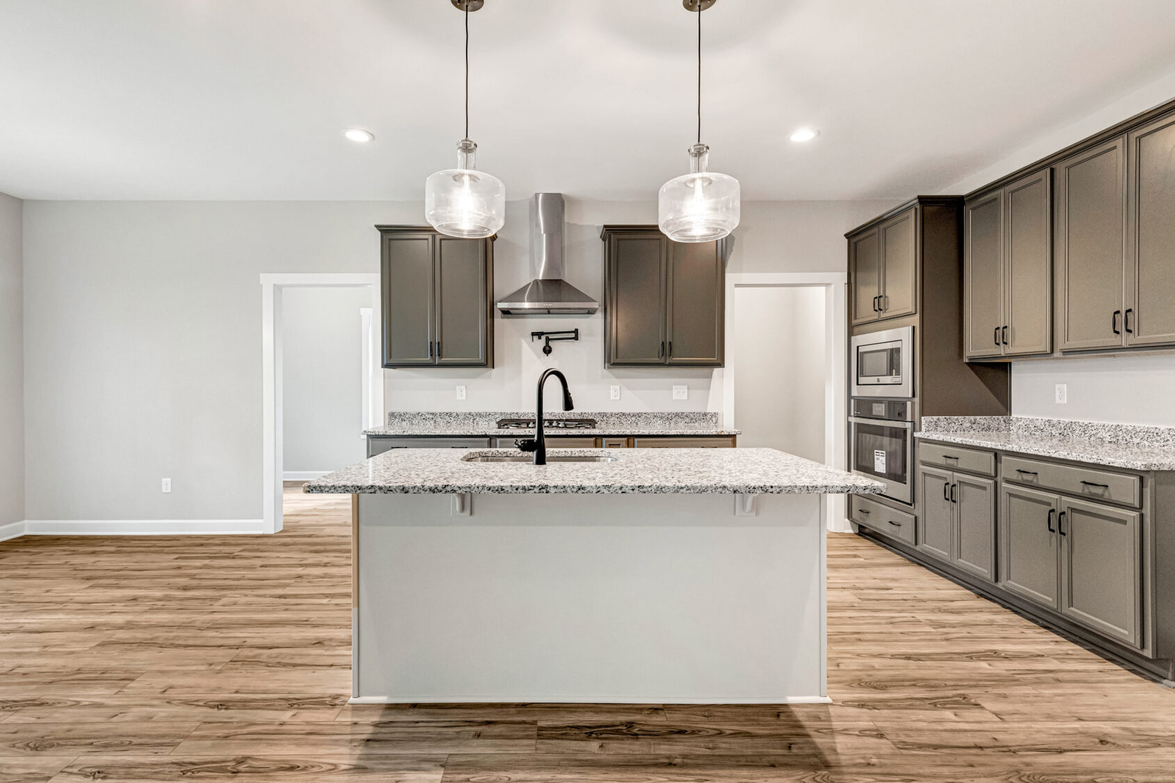 Modern kitchen with gray cabinets, granite countertops, island, and pendant lights on wood flooring.
