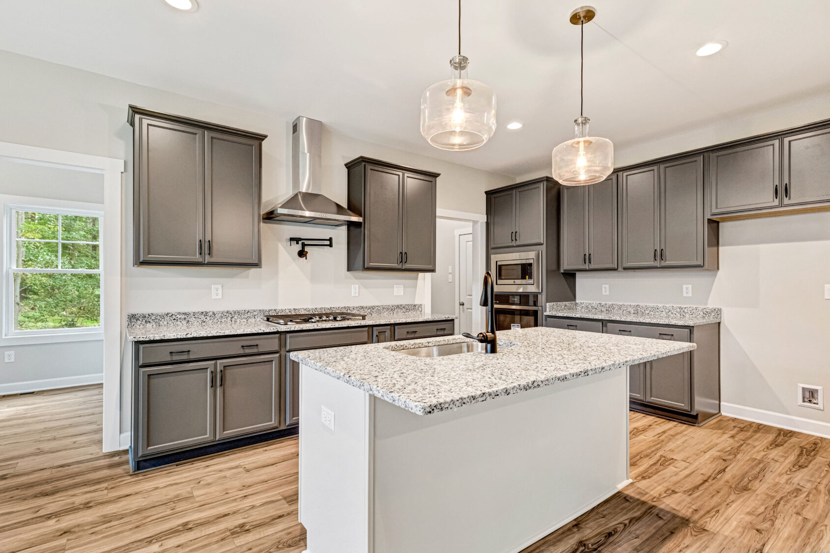 Modern kitchen with gray cabinets, granite countertops, pendant lights, and wood flooring.