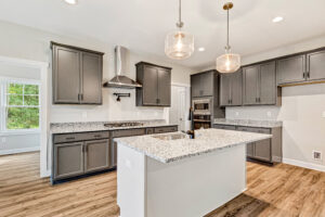 Modern kitchen with gray cabinets, granite countertops, pendant lights, and wood flooring.