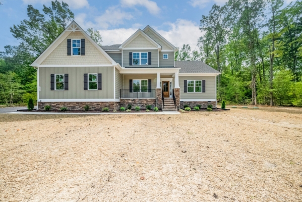 Two-story new home with beige siding and stone accents, nestled among trees and a freshly landscaped yard.