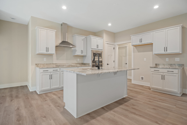 A modern kitchen in a new Richmond home with white cabinets, marble countertops, and a central island on light wood floors.