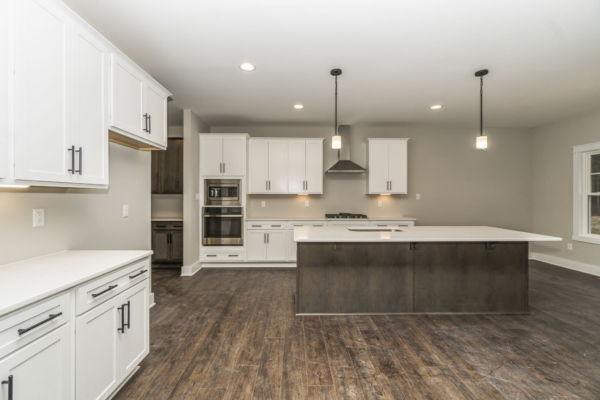 Modern kitchen in a new home with white cabinets, wood flooring, central island, pendant lighting, and grey walls.