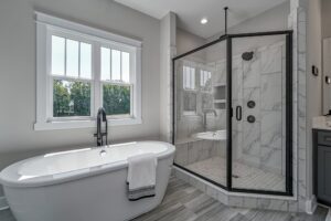 Modern bathroom in a new home features a freestanding tub, gray tile floor, and glass-enclosed shower by the window.