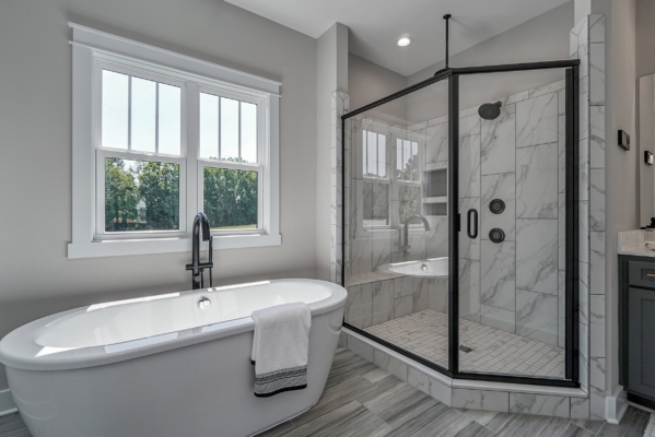 Modern bathroom in a new home features a freestanding tub, gray tile floor, and glass-enclosed shower by the window.