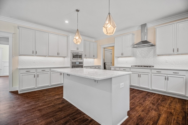 Modern kitchen in new Richmond home with white cabinets, marble island, wood floor, and geometric pendant lights.