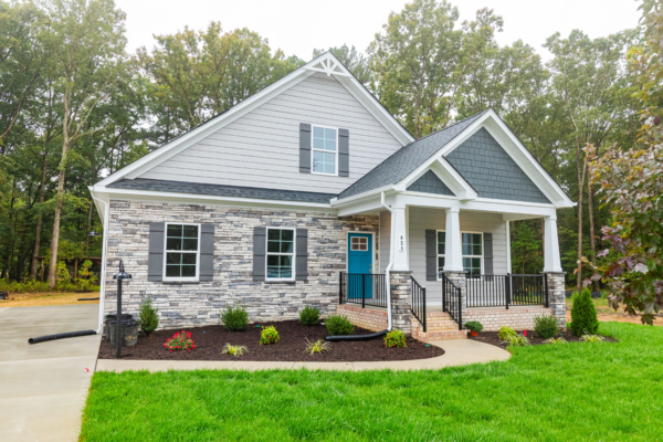 Modern new home with brick and stone exterior, front porch, black railing, surrounded by trees and a landscaped lawn.