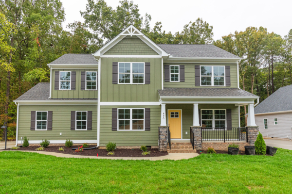 Charming two-story green house in Richmond with a porch, white trim, yellow door, and surrounded by lush greenery.