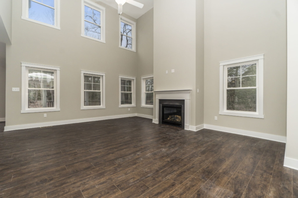 Spacious room in a new home with high ceilings, dark wooden floor, large windows, and a fireplace.