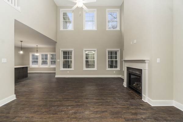 Spacious living room with high ceilings, large windows, and a fireplace in a new home with an open view to the dining area.