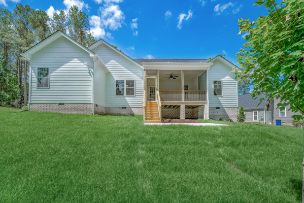 Single-story white house in Richmond with a wooden porch, surrounded by green grass and trees under a blue sky.