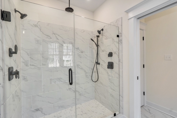 A modern bathroom in Scotchtown Estates boasts a glass-enclosed marble shower with two black rainfall showerheads, offering a touch of luxury and elegance.