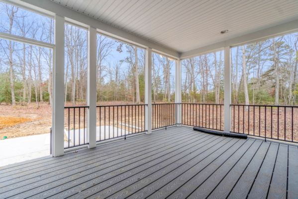 Covered porch with wooden flooring, overlooking a forest of bare trees and clear skies in a new home.