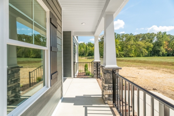 A porch with pillars overlooks a green field and trees under a clear blue sky in new homes in Richmond.
