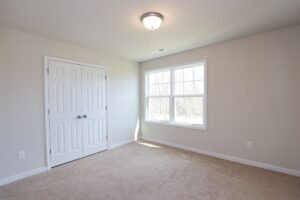 Empty bedroom in new homes in Richmond VA with beige carpet, light walls, double-door closet, and natural light.