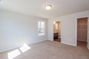 Bright empty bedroom with beige carpet, two windows, and access to bathroom and walk-in closet—ideal for new homes in Richmond VA.