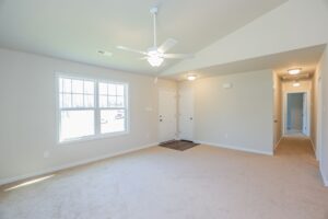 Bright empty living room with beige carpet, white ceiling fan, and windows—ideal for new homes in Richmond VA.
